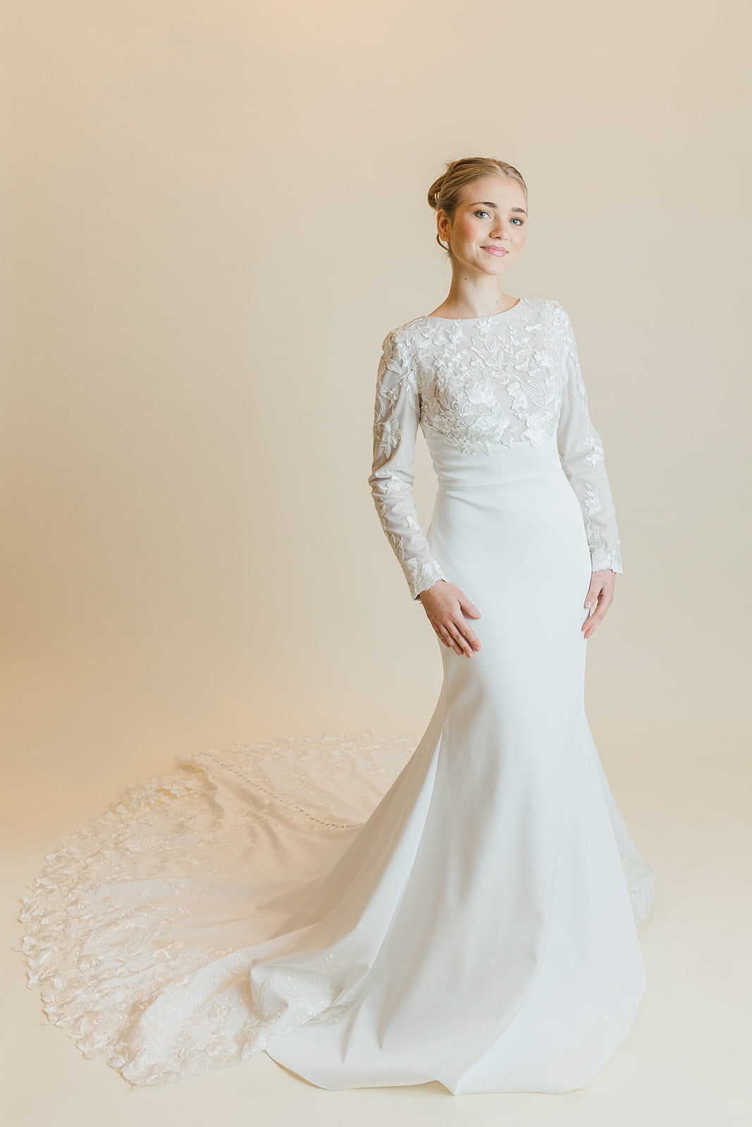 A woman wearing a modern style long sleeve white wedding dress with a square neckline and buttons extending to the train of the dress.